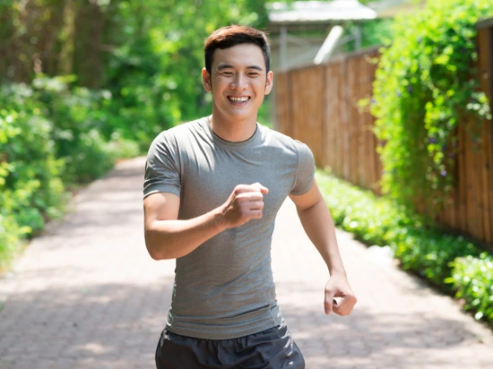 A happy young man taking a slow jog in order to achieve 10,000 steps daily.