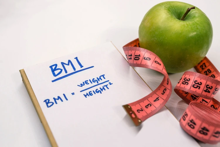 Formula of BMI written on a notepad with an apple and measuring tape beside.