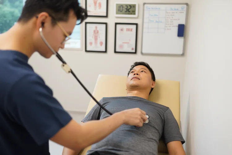Doctor examining male patient using stethoscope for pre-employment medical check-up in Singapore.