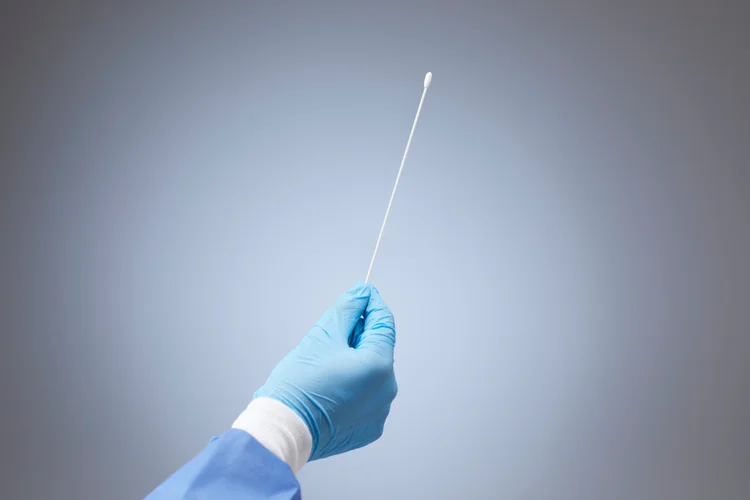 Gloved hand holding sterile swab used for vaginal sample collection to test for bacterial vaginosis.