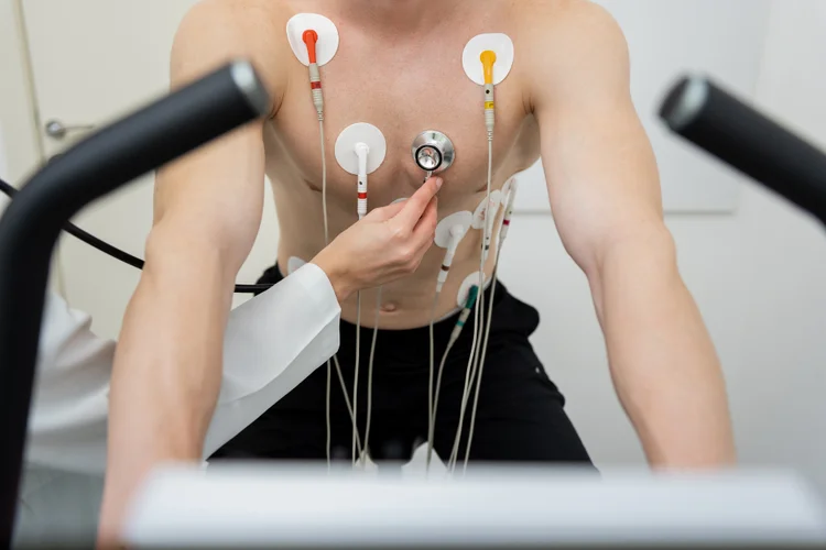 Male patient preparation for treadmill stress test with electrodes being attached to monitor heart rhythm and ECG activity.