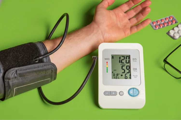 Person using digital blood pressure monitor at home showing healthy reading of 120 over 59 mmHg.
