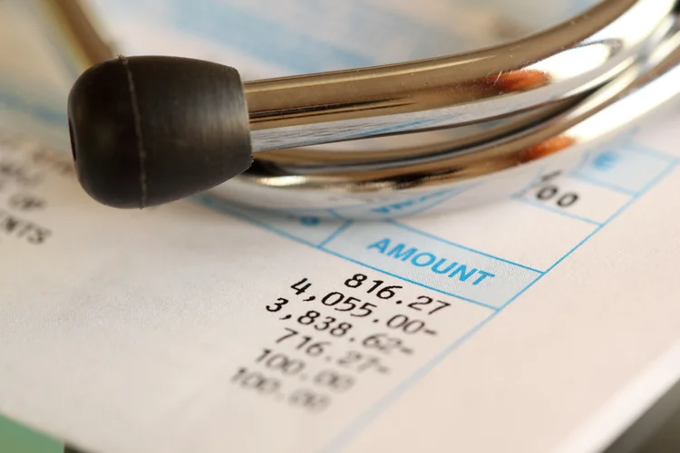 Stethoscope on bill showing health screening cost affected by type, quantity and complexity of tests.