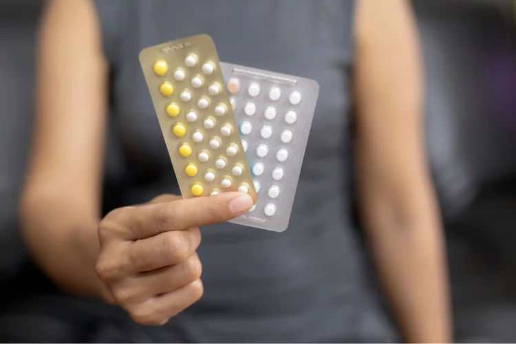 Woman holding up two different types of combined oral contraceptive pill (COCP) blister packs.