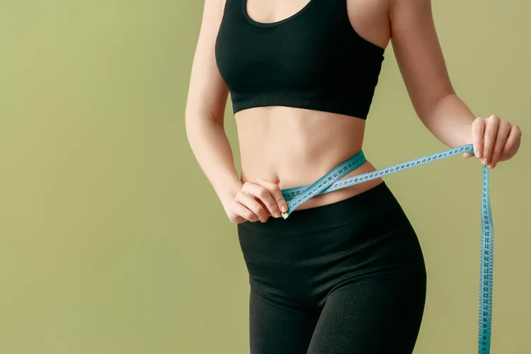 Woman measuring waist with tape measure to track progress in weight management and fat loss.